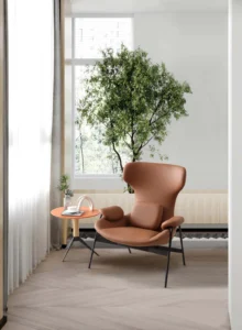 Brown LC24-04 lounge armchair with a curved high back, padded armrests and dark exposed legs beside a window
